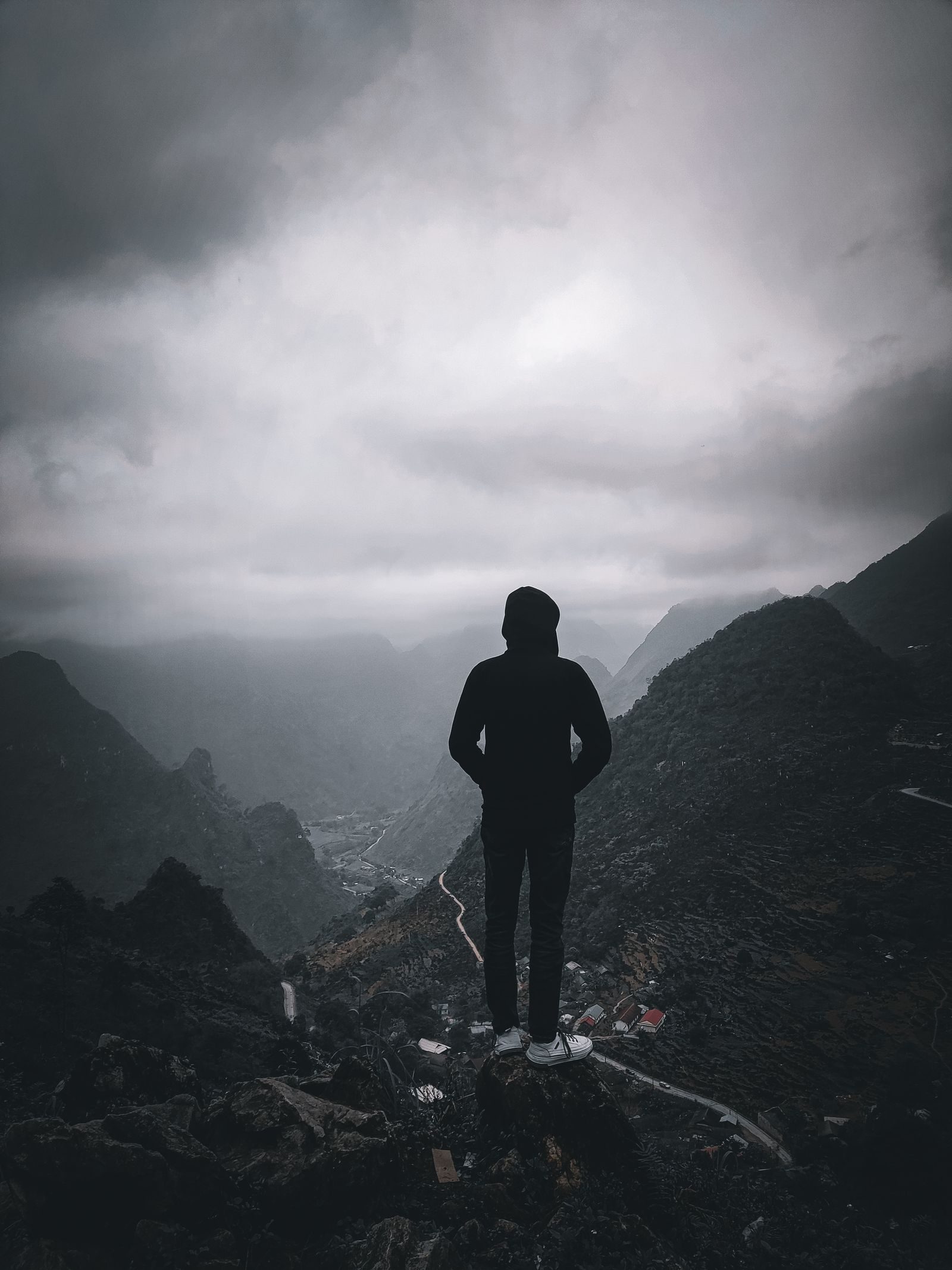 A hiker in a hooded jacket looking out over a fog-covered mountain valley